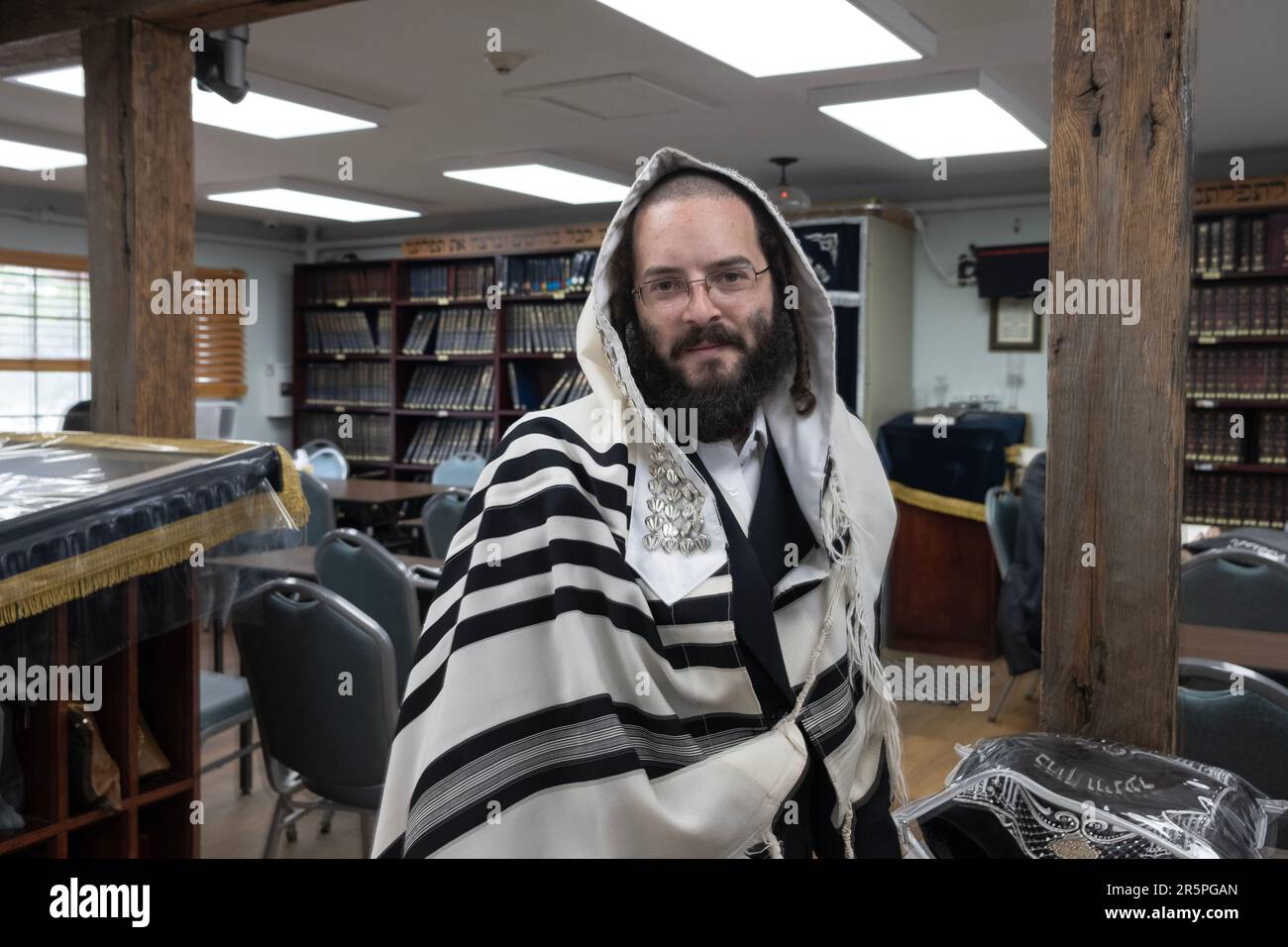Posed portrait of an orthodox Jewish man in an empty synagogue wearing