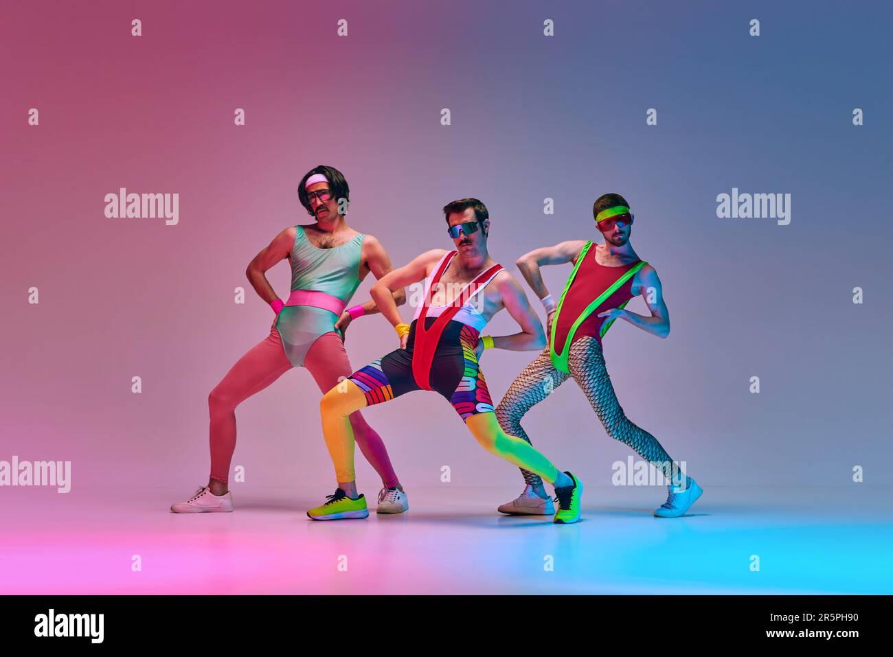 Funny men in vintage, colorful sportswear posing, doing aerobics exercises  against gradient blue pink studio background in neon light Stock Photo -  Alamy
