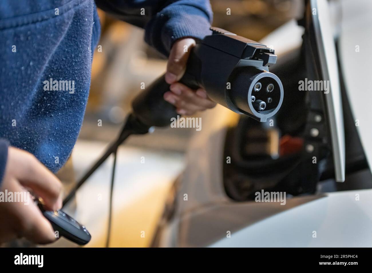 Woman hands holding electric car charger and remote controller, ready to connect to electric vehicle at home garage. Stock Photo