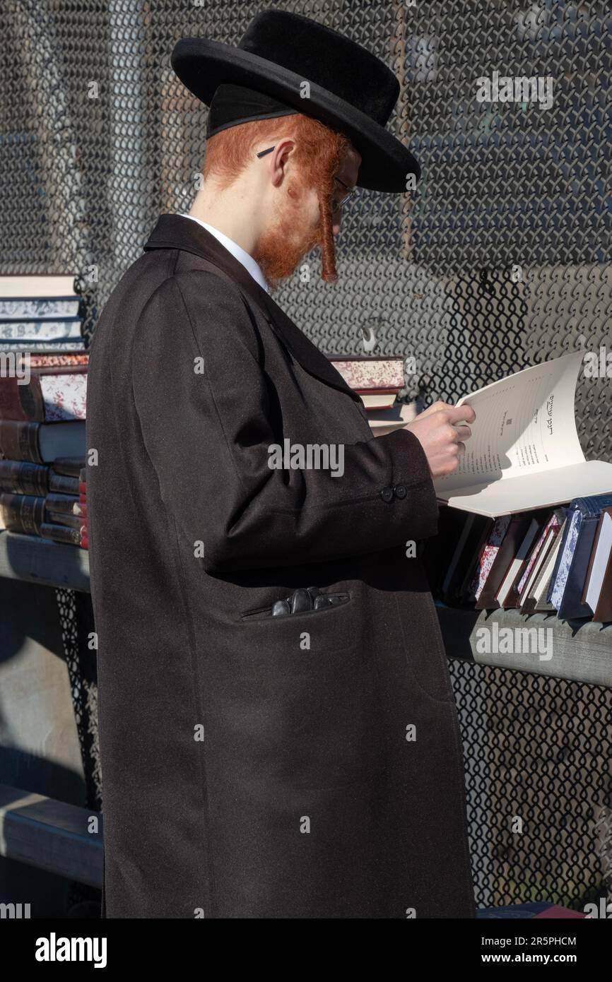 A hasidic Jewish redhead with long curly peyus shops for religious books at a pop up store on Lee Avenue in Wiliamsburg, Brooklyn, New York City. Stock Photo