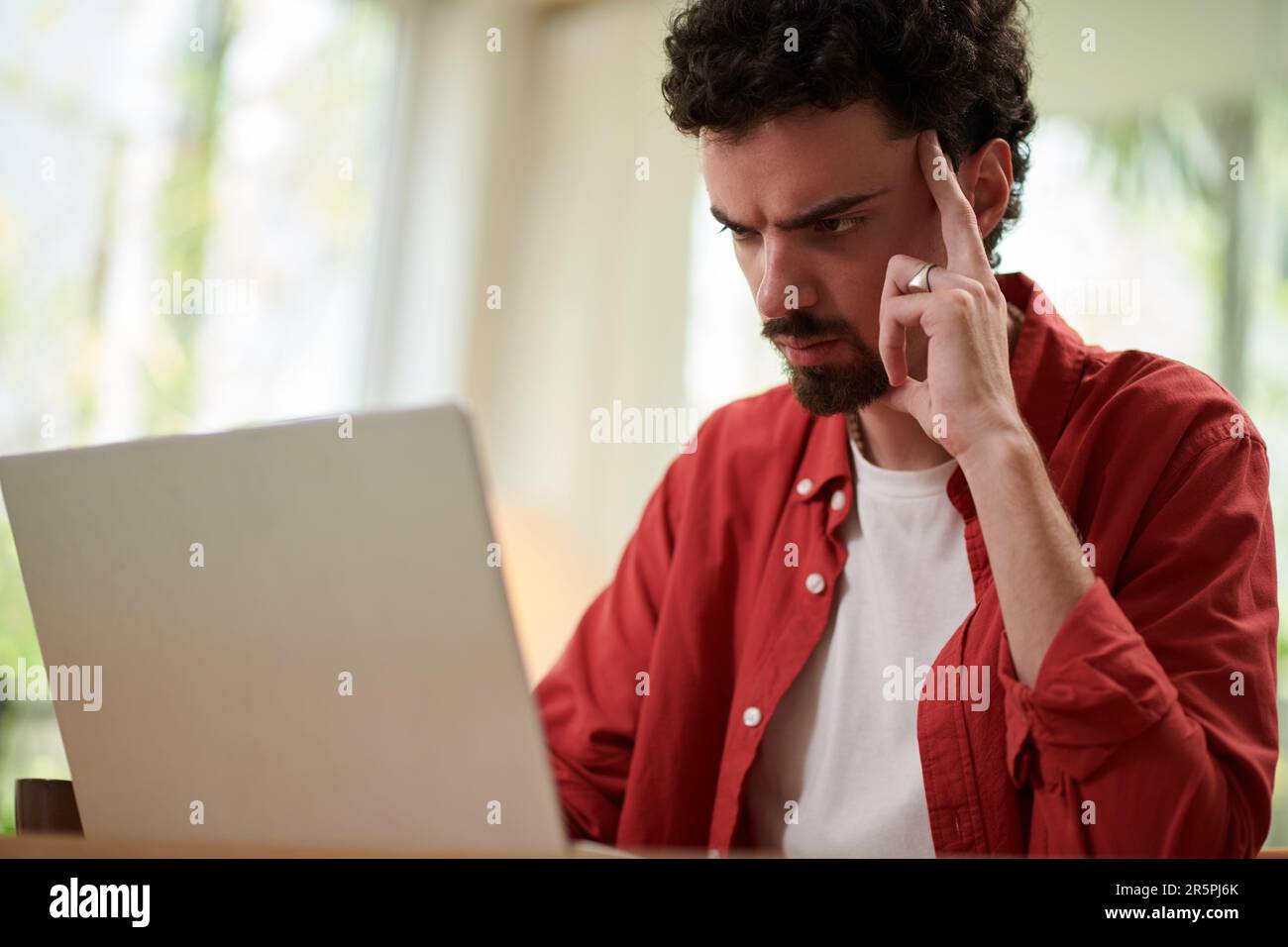 Pensive frowning man reading programming code on laptop screen Stock Photo