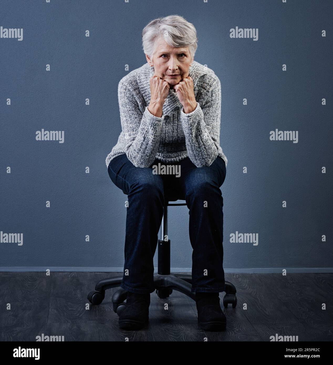 If looks could kill. Studio shot of an elderly woman sitting with her hands under her chin while looking at the camera. Stock Photo