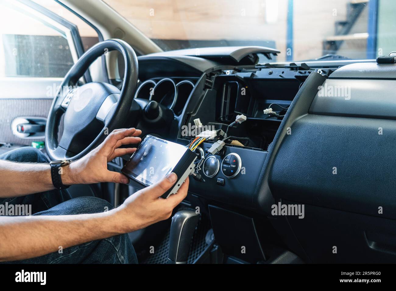Auto in Car Service, process of installing modern 2-din radio sound system. Auto electric hands on dashboard fixing problem close-up. Stock Photo