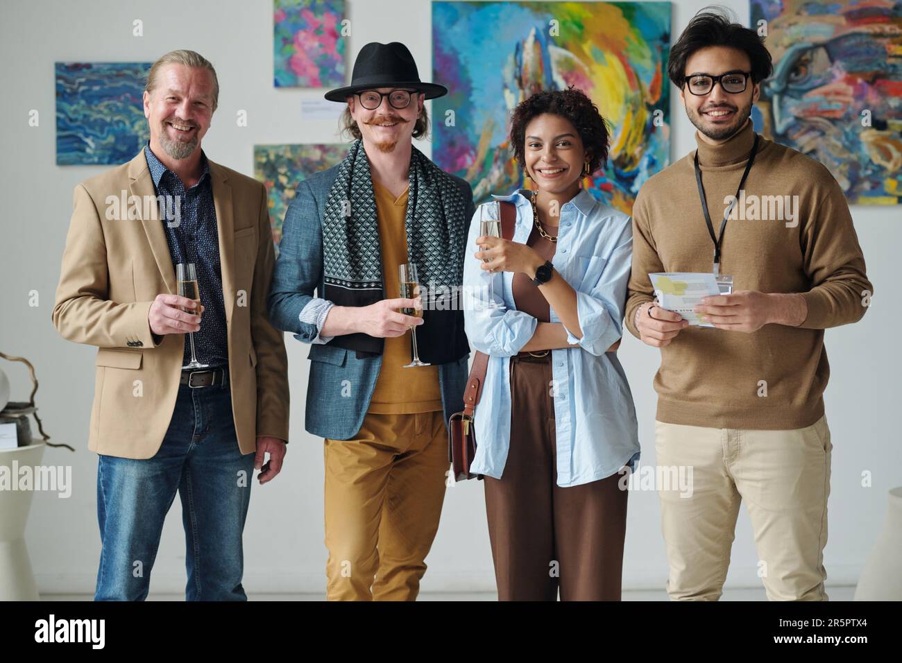 Portrait of group of people smiling at camera standing with glasses of champagne in art gallery Stock Photo
