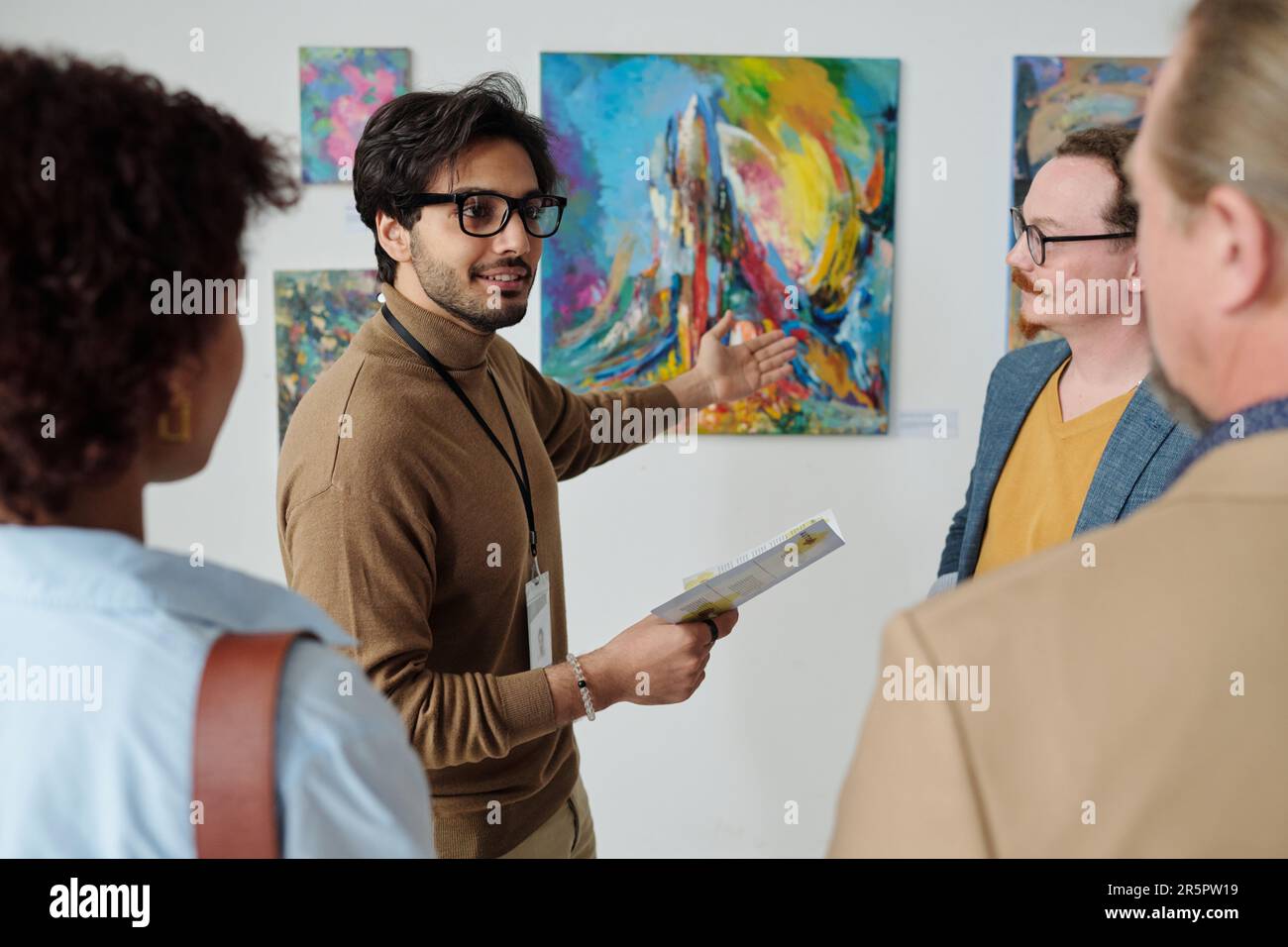 Young guide pointing at paintings on the wall and talking about modern ...