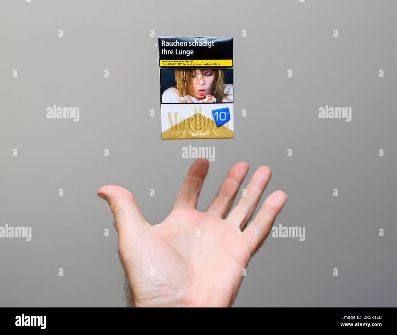Paris, France - May 30, 2023: Hand about to catch a Marlboro cigarette pack wich is floating levitating in the air against gray background - unhealthy life concept for damage to health Stock Photo