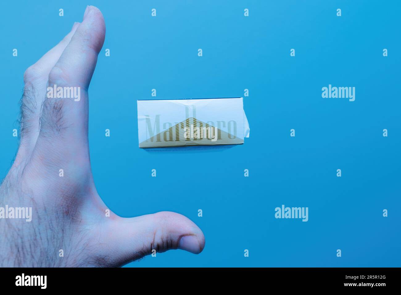Paris, France - May 30, 2023: Someone is reaching for a Marlboro pack floating in the air against a blue background. A concerning commentary on unhealthy habits and tobacco use. Stock Photo