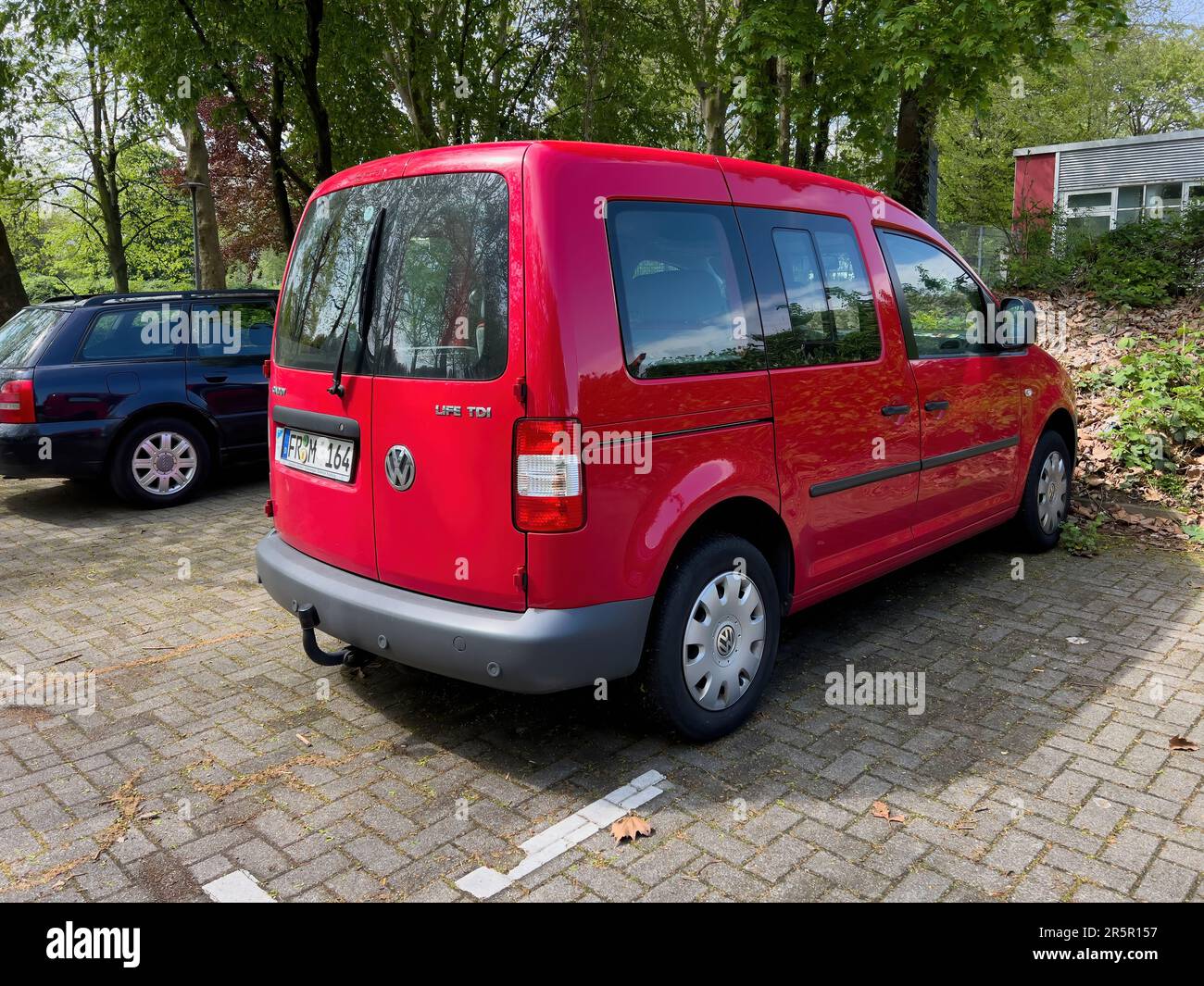 Kehl, Germany - May 1, 2023: Green commuting with a red VW Caddy Life TDI model parked by a tree. Its diesel motor is eco-friendly Stock Photo