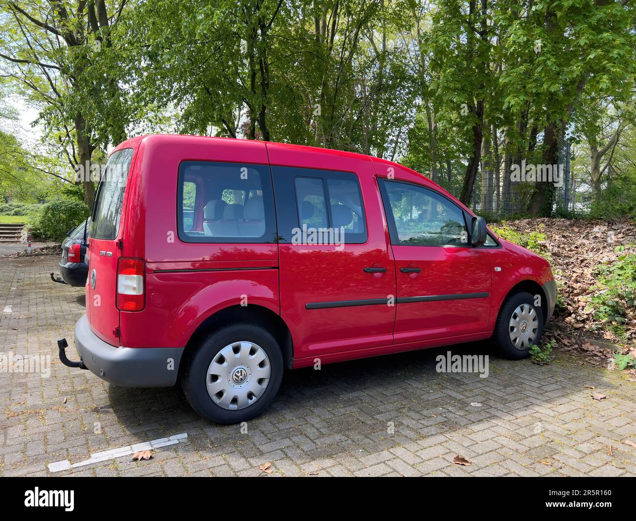 Kehl, Germany - May 1, 2023: A red VW Caddy Life is parked under a large tree amidst greenery. Its a diesel TDI model motor vehicle, perfect for commuting in traffic. Stock Photo