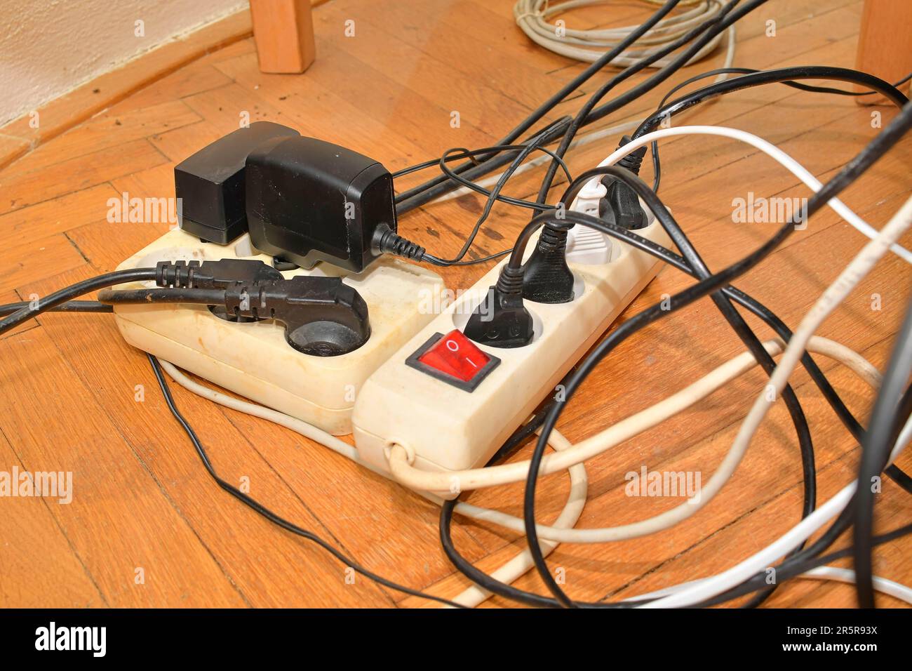 Tangled cables on the parquet floor. Overloaded electrical boards on