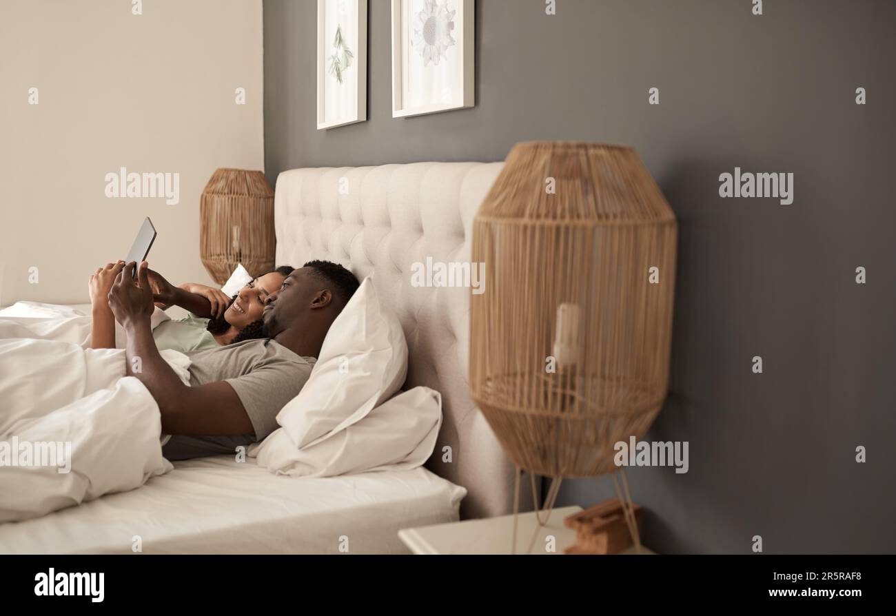 Smiling multiracial couple using a digital tablet in bed Stock Photo