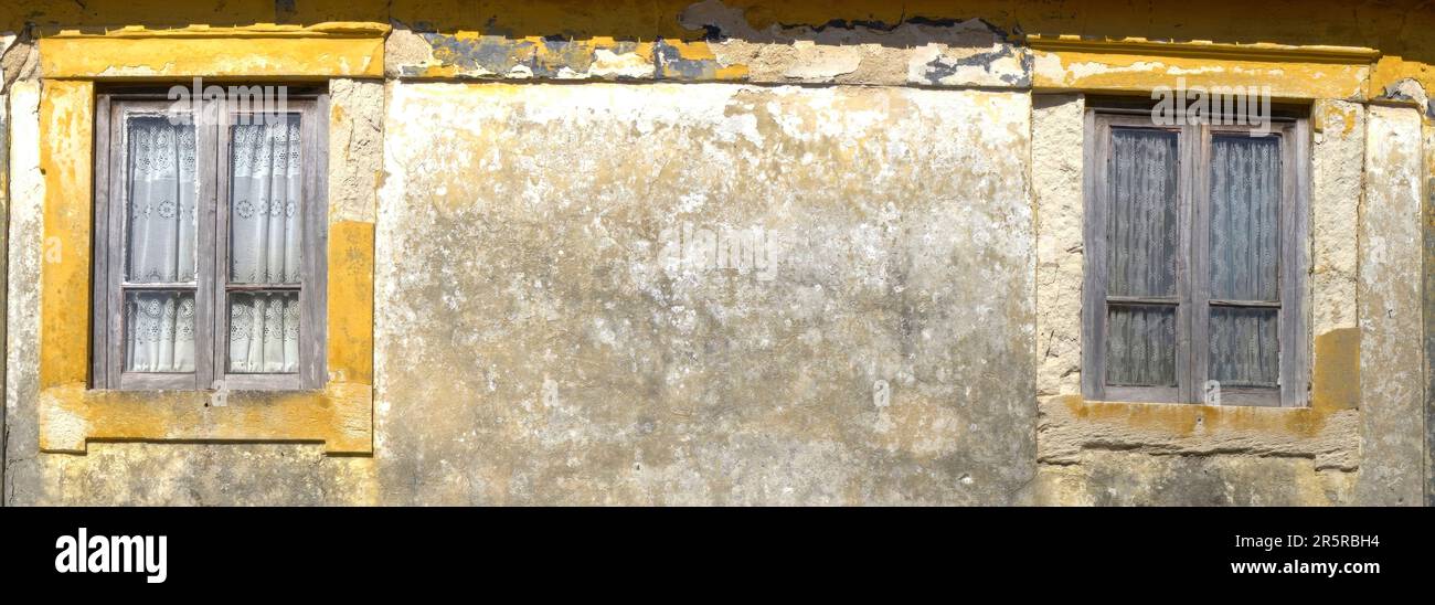 Quiaios, Portugal - August 14, 2022: Close up of windows of old dilapidated house painted yellow showing timber frames and curtains Stock Photo