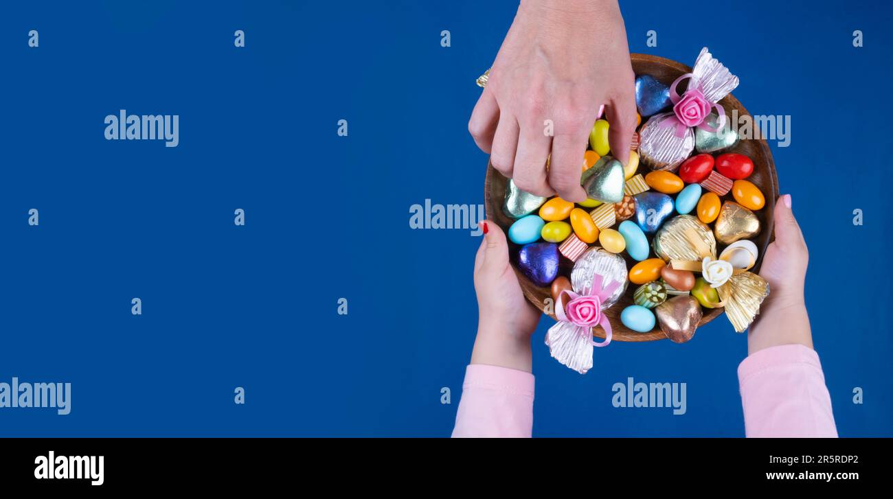 Top view image of woman and child hand holding bowl of candies. Isolated dark blue background, copy space. Ramadan feast celebration concept idea. Stock Photo