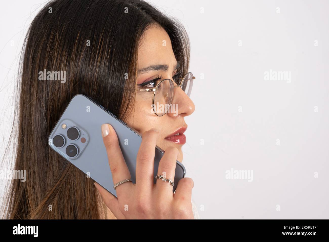 Close up side view image of woman talking on the phone. Holding modern blue three camera smartphone. Seriously looking copy space. Stock Photo