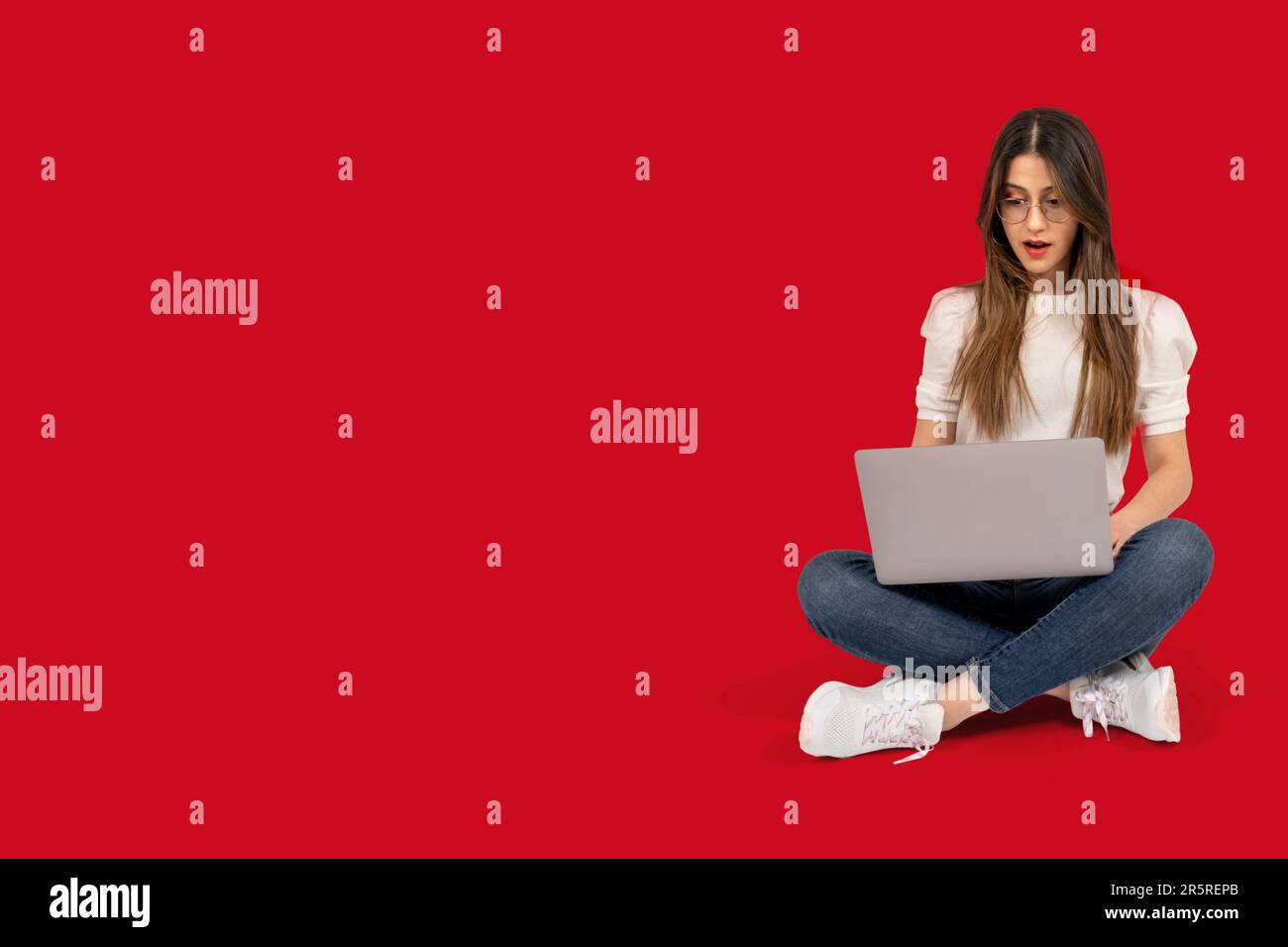 Full body length view of shocked woman. Brunette young girl sitting on the ground. Holding laptop looking screen surprised what she see. Stock Photo