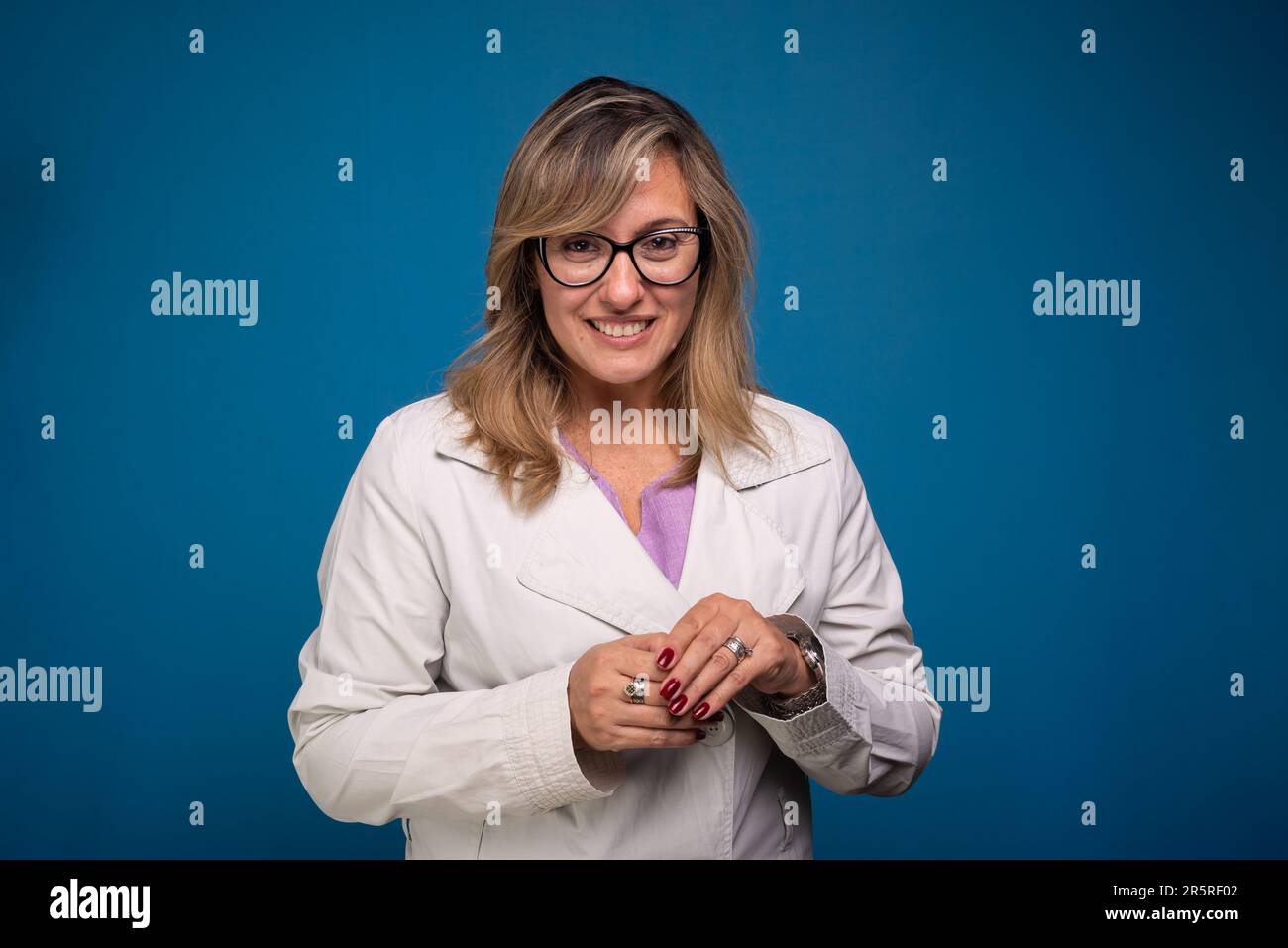 Confident female doctor dressed in beige coat, wearing glasses and smiling. Positive person. Isolated on blue background Stock Photo