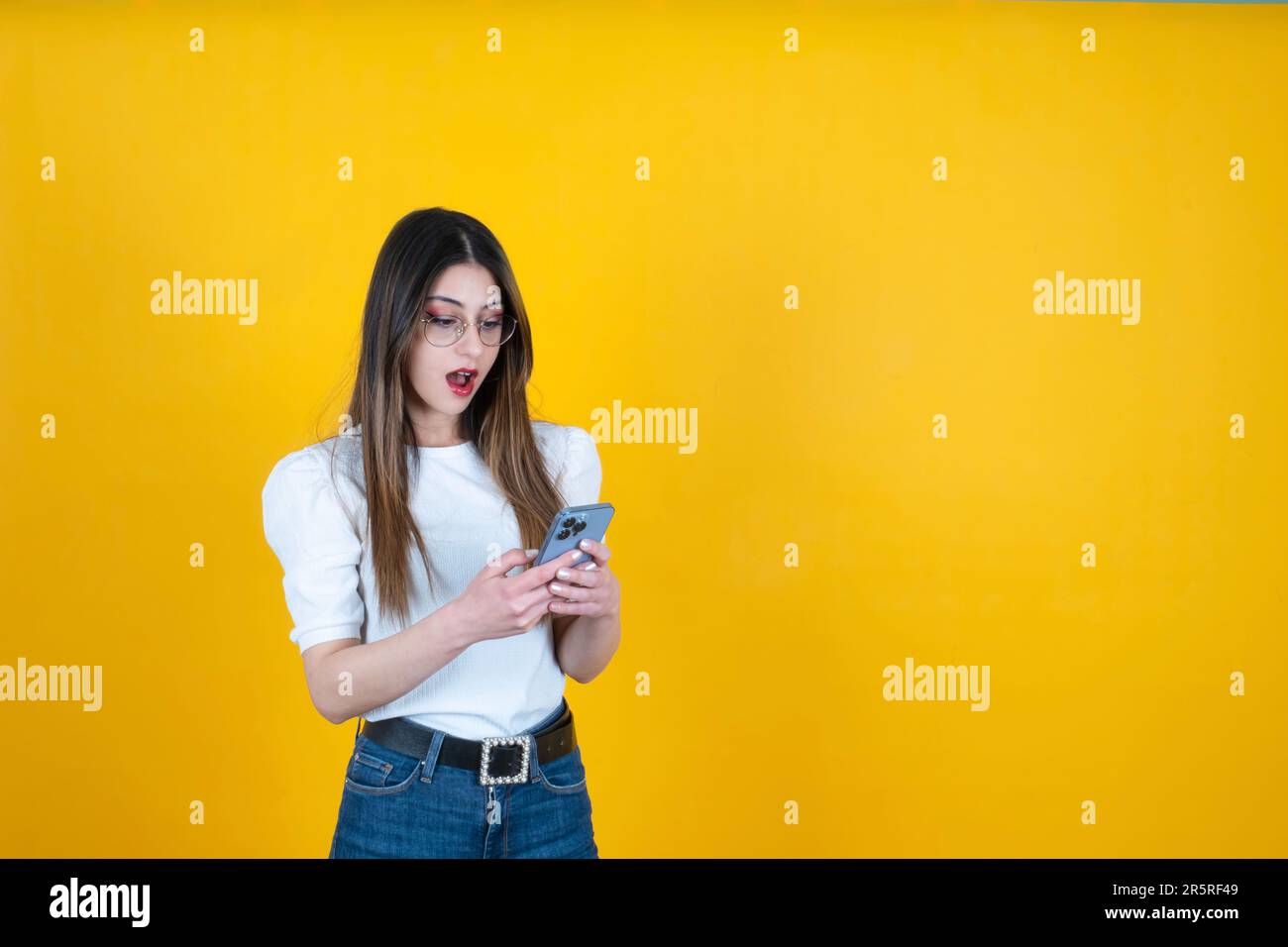 shocked woman. Surprised caucasian girl holding and using smartphone. Browsing social media, reading a message, emotional young lady facial expression Stock Photo