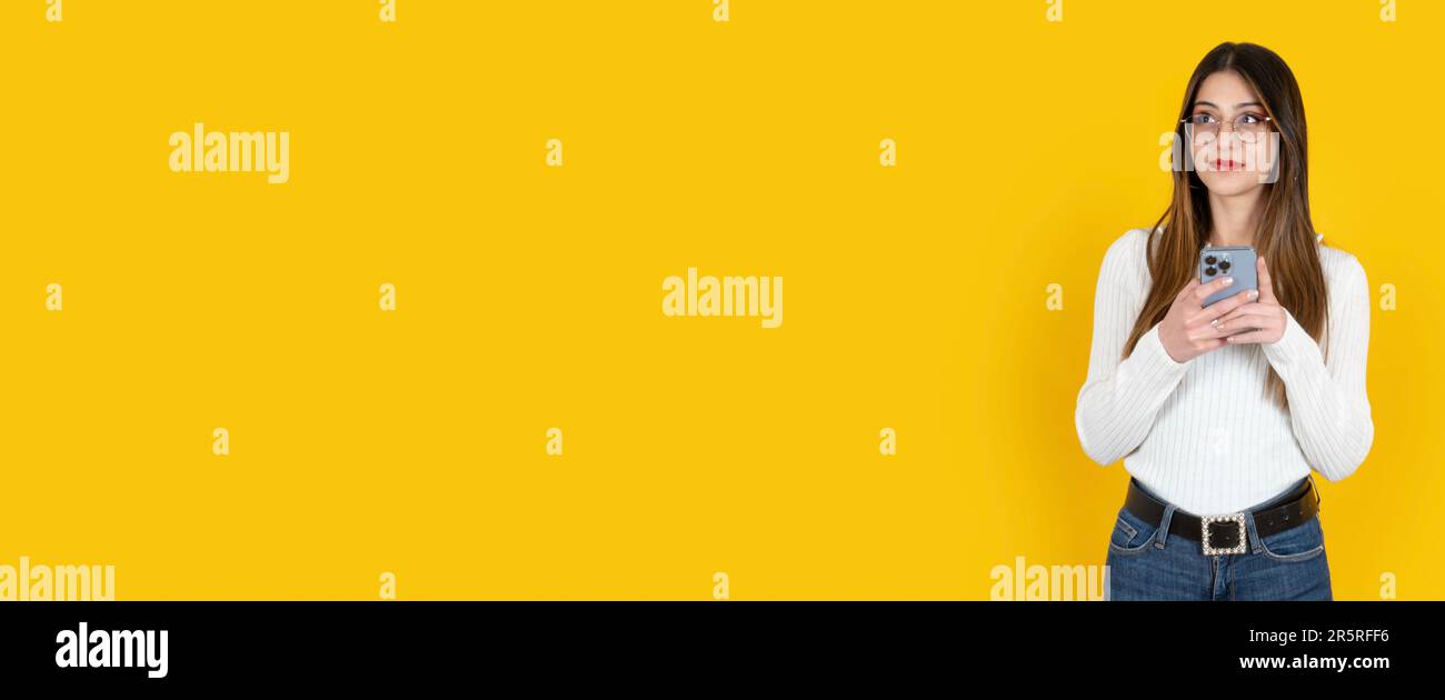 Woman using smartphone. Looking aside on copy space banner design template idea. Yellow studio background. Thinking long brown haired lady. Stock Photo