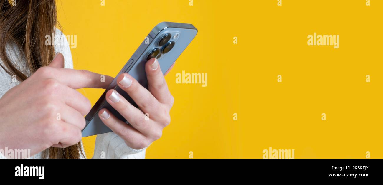 Focus on woman hand using smartphone. Finger touching screen, browsing internet, searching social media, messaging. Isolated yellow background. Banner Stock Photo