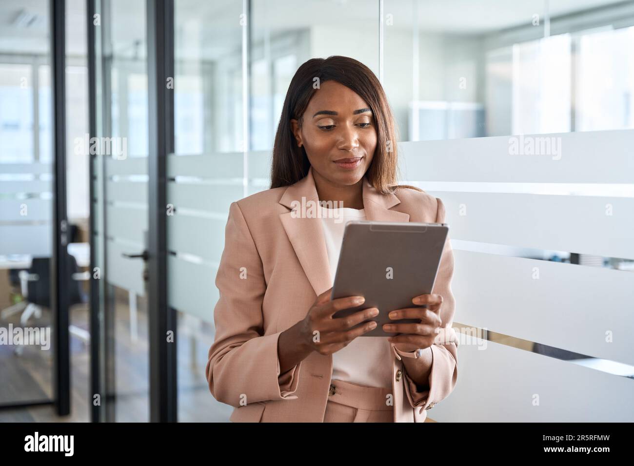 Young busy African American business woman using tablet standing in office. Stock Photo
