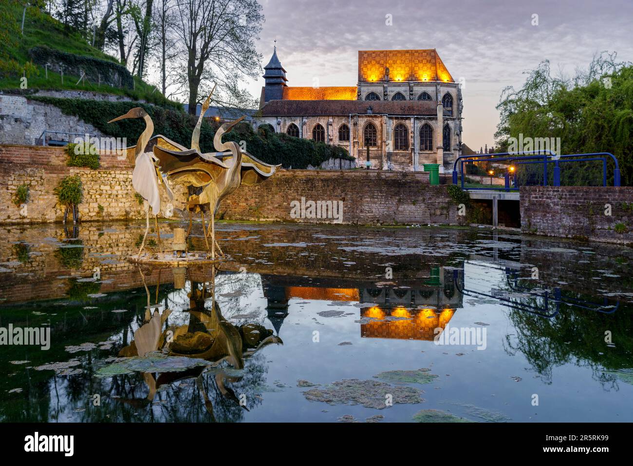 France, Seine-Maritime, Elbeuf-sur-Seine, designated as French Towns and Lands of Art and History, Puchot district, reflection of the Saint-Etienne church and resurgence of the stream named Puchot, in the René Youinou Garden, also called Spring Garden, sculpture by Nicolas Popelin, named The Three Herons Fountain Stock Photo