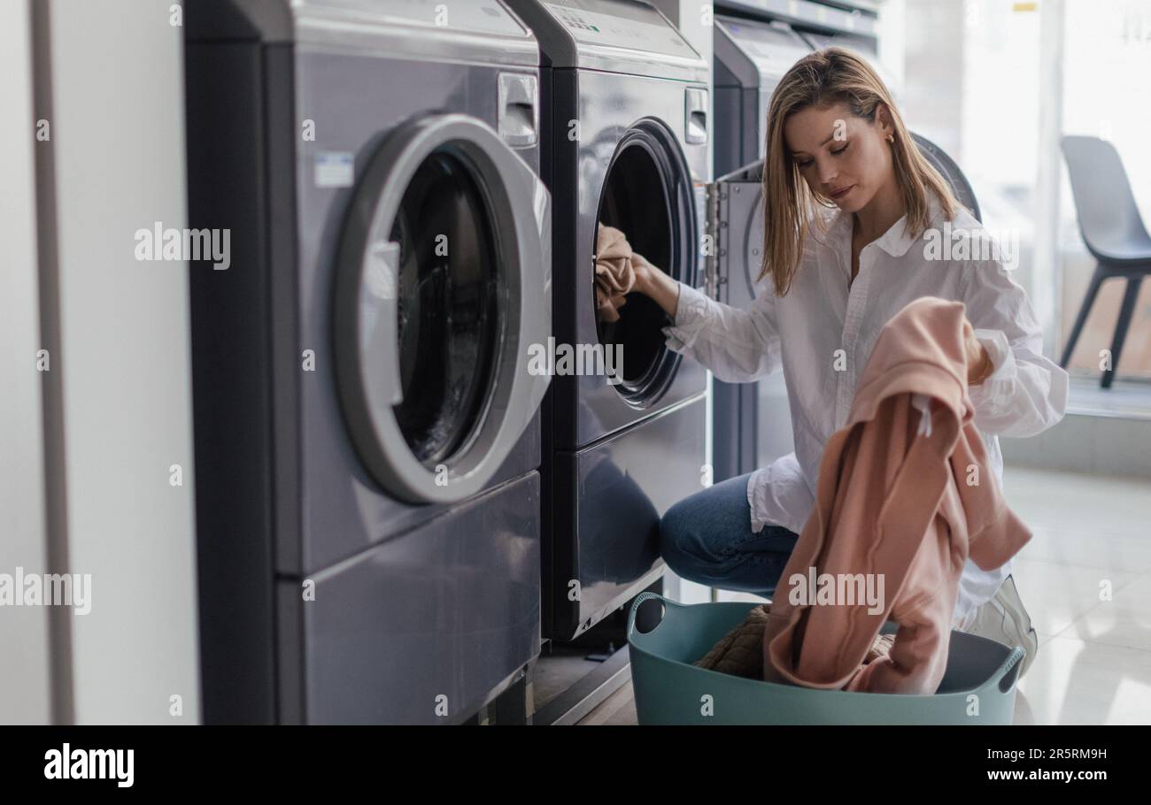 Young woman loading washing machine in public laundry. Stock Photo