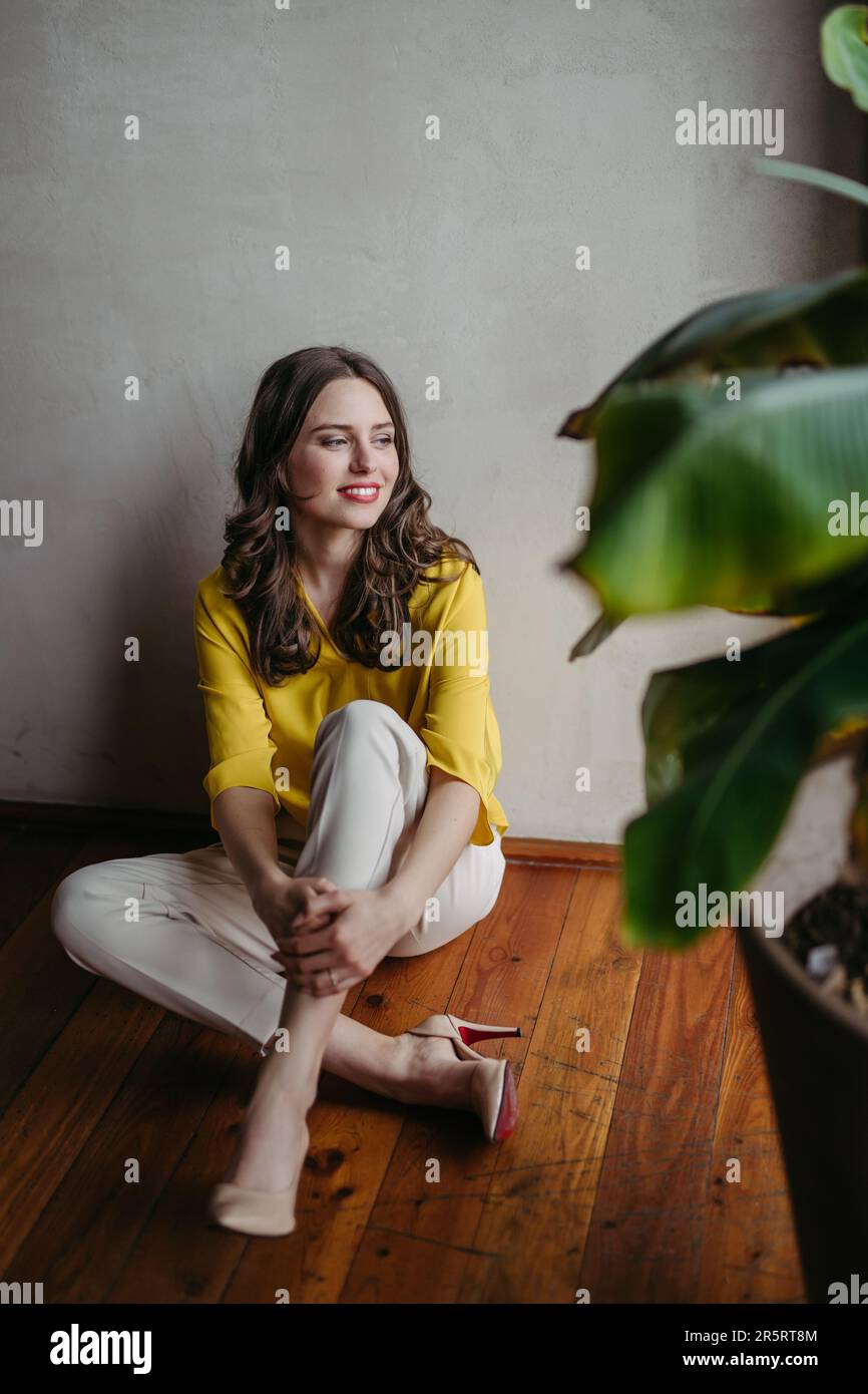 Portrait of beautiful young woman sitting near window in room full of plants. Stock Photo