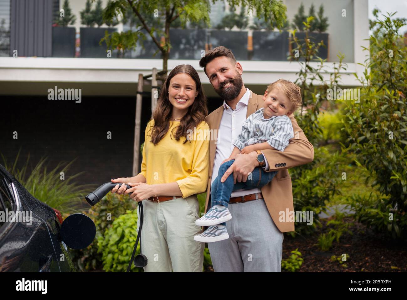 Happy young family with little son charging their electric car. Stock Photo