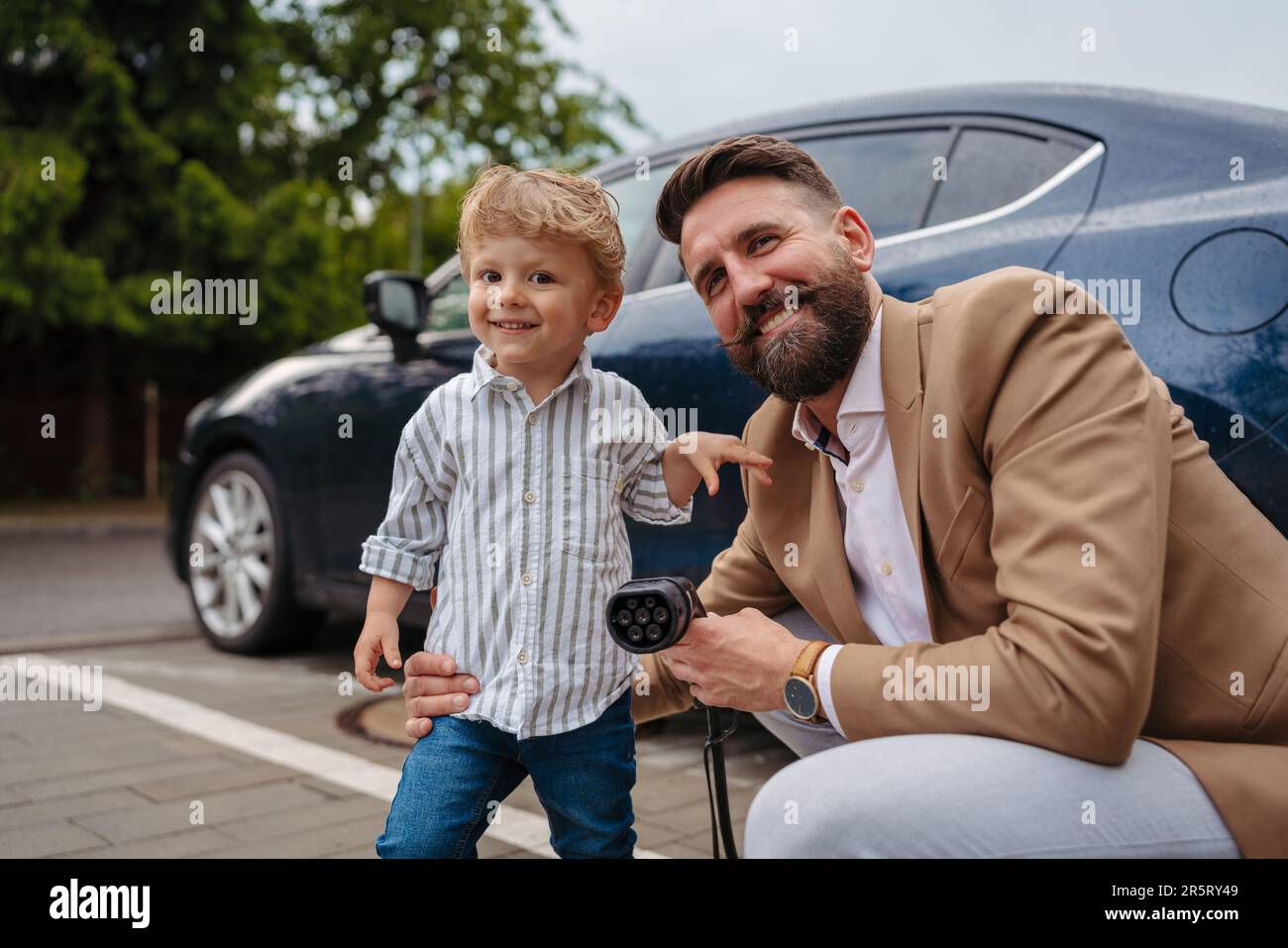 Close up of man and his little son holding power supply cable from their electric car. Stock Photo