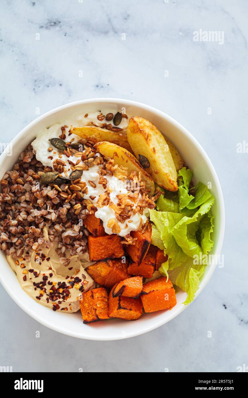 Vegetarian buddha bowl with buckwheat, cottage cheese, hummus and baked sweet potato, top view. Balanced food concept. Stock Photo