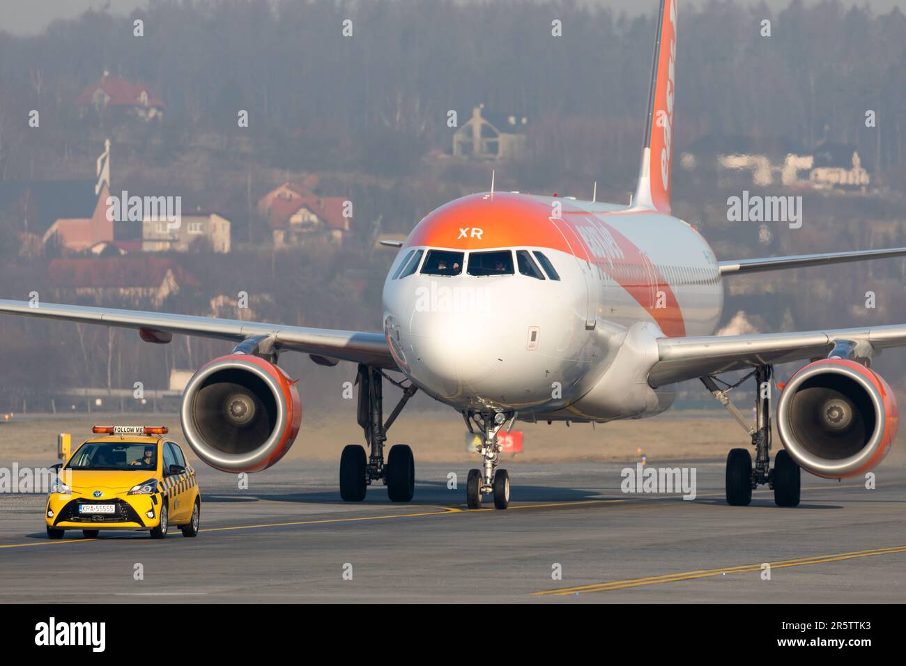 An orange and white single engine jet is parked on a runway next to a large truck Stock Photo