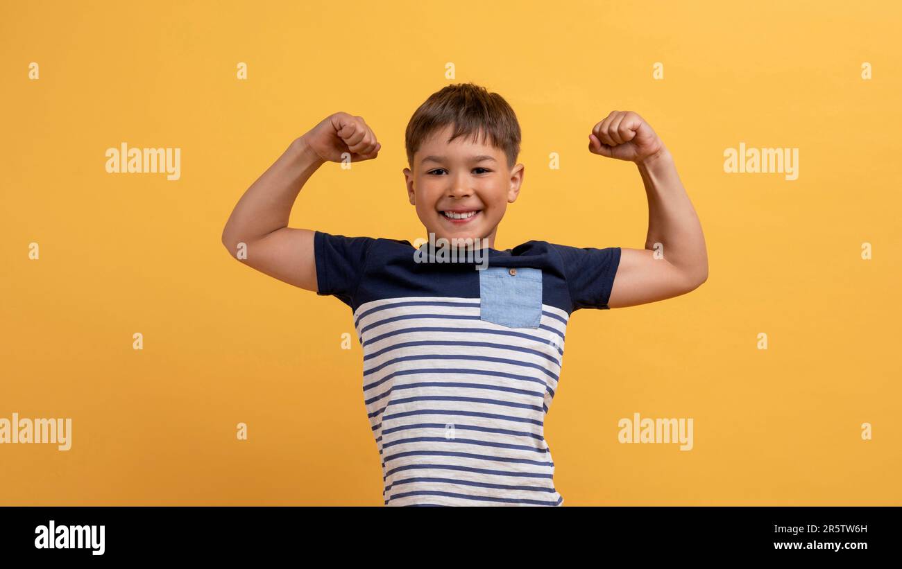 Funny cute boy showing his strong hands, yellow background Stock Photo