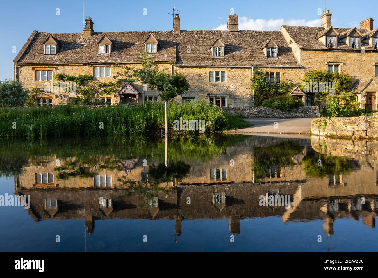 Evening sun shines on the River Eye and traditional honey-coloured Cotswold stone cottages in Lower Slaughter Village in Gloucestershire, England. Stock Photo
