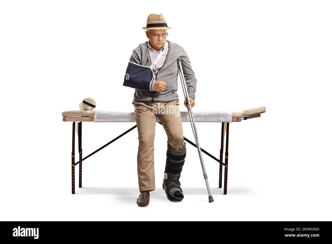 Senior man with a broken arm and leg sitting on a bed for physical