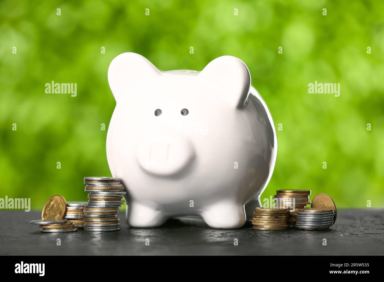 Piggy bank with coins on table against blurred green nature background ...