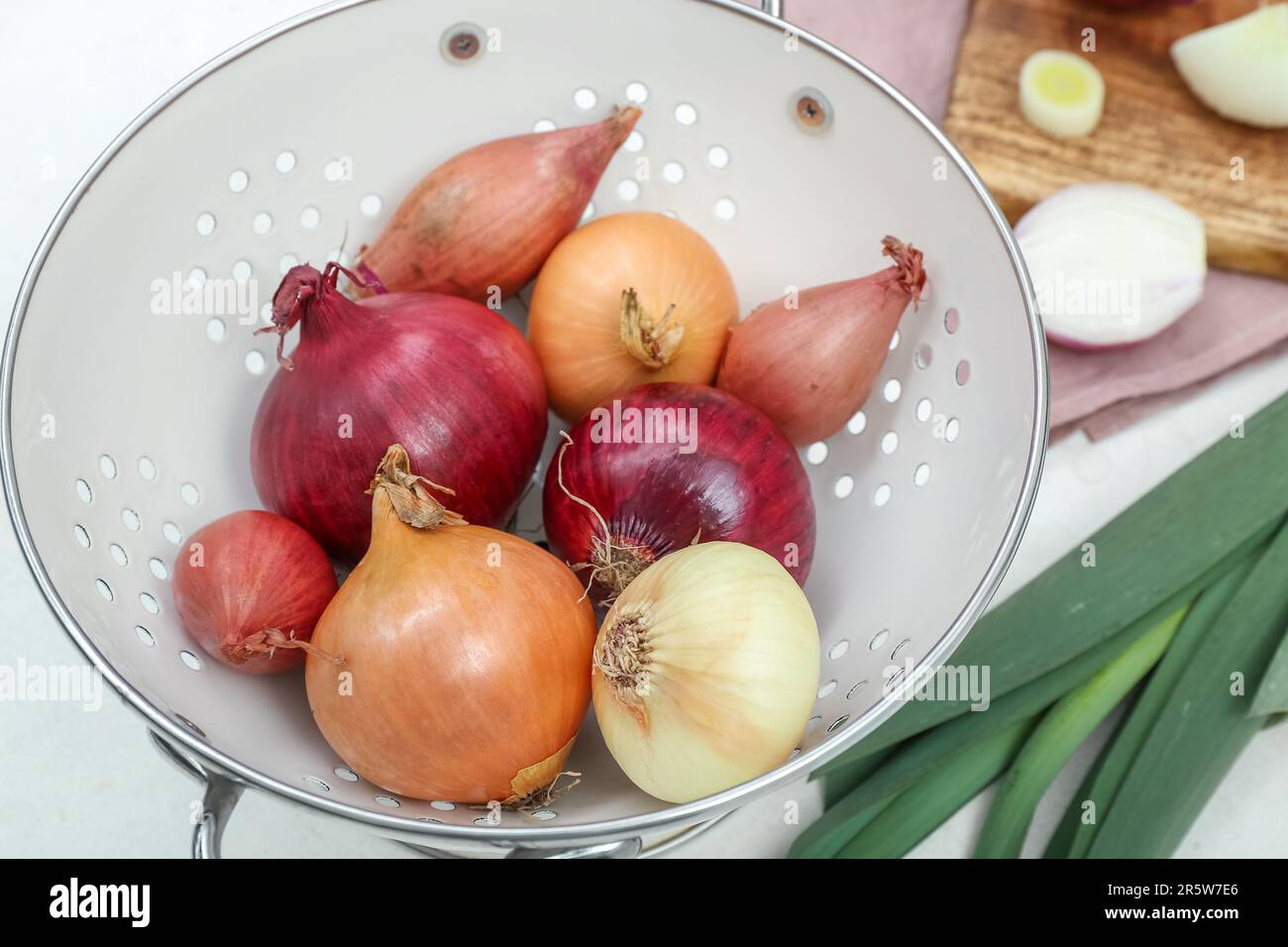Wooden board and colander with different kinds of onion on white ...