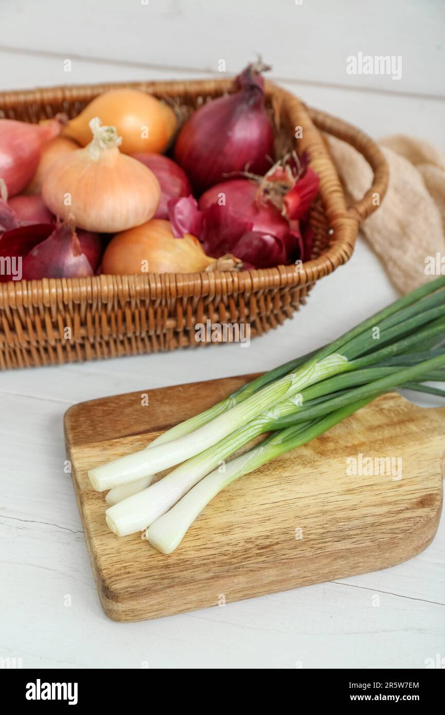 Board and wicker basket with different kinds of onion on white wooden ...