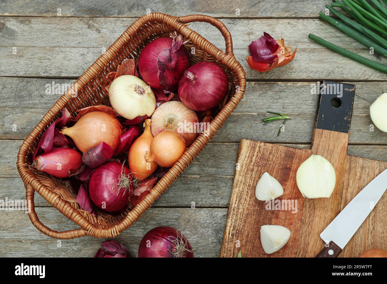 Board and wicker basket with different kinds of onion on brown wooden ...