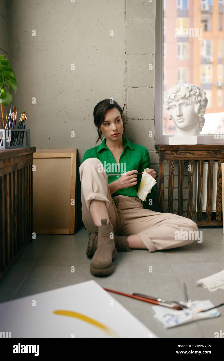 Relaxed young woman artist sitting on floor front of drawing ...