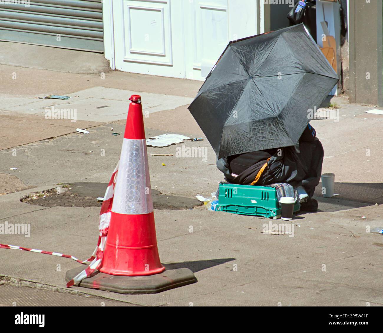 homeless begging with an umbrella as a parasol with the iconic symbol of the city a traffic cone Stock Photo
