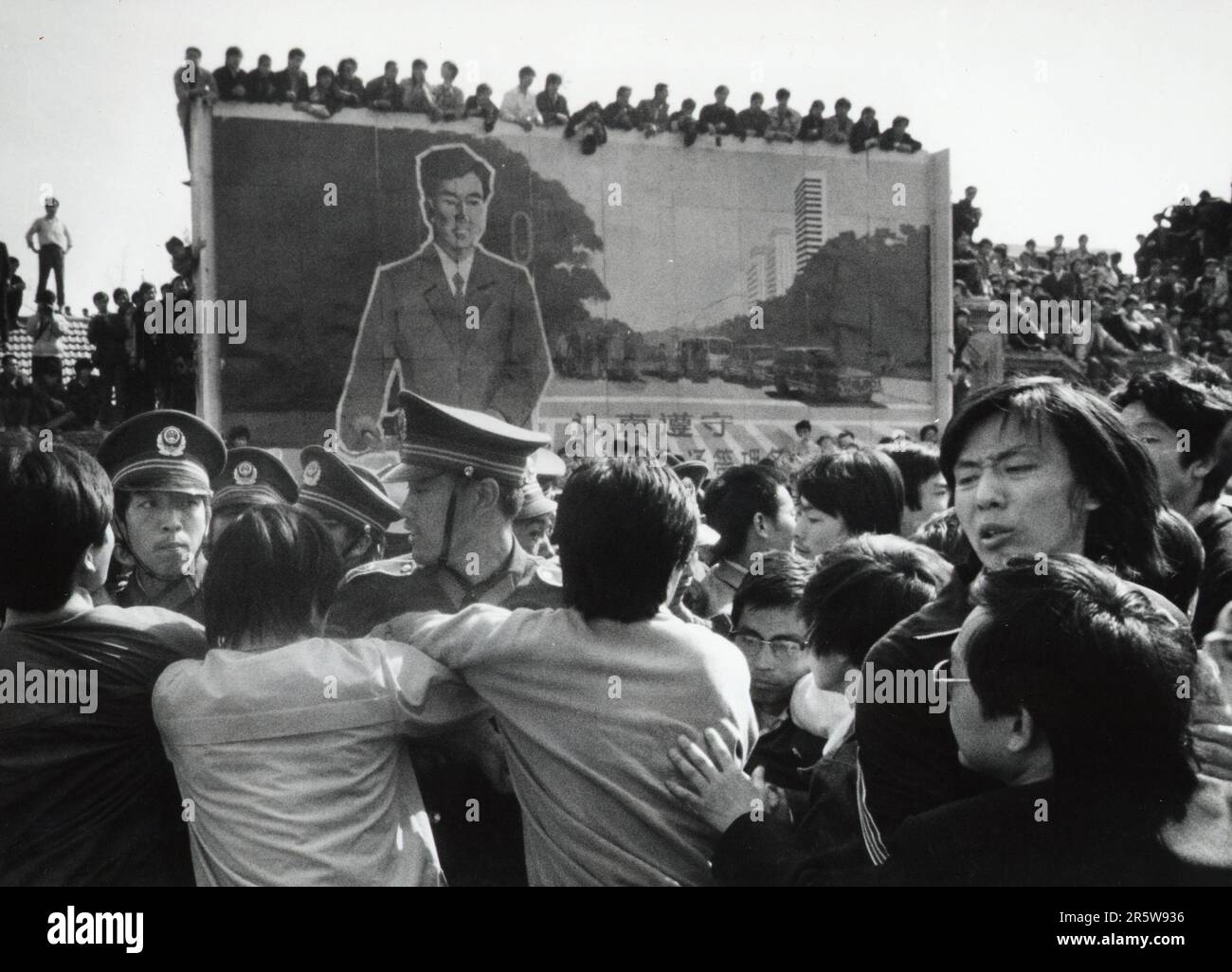 Chinese pro-democracy protesters break through police lines on their way to Tiananmen Square on April 27 1989 as crowds of onlookers view the scene from atop a traffic safety billboard. Stock Photo