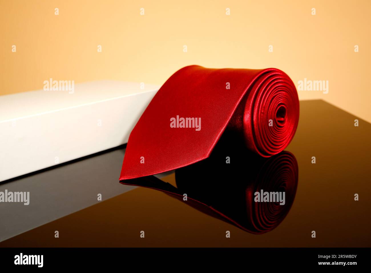 A close-up image of a solid red necktie lying on a black reflection surface Stock Photo