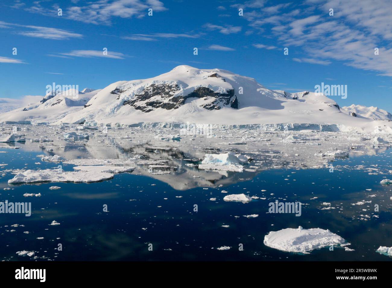 Glacial mountainscape featuring a pristine lake with a few ice cubes floating on its surface, framed by snow-capped peaks in the background Stock Photo