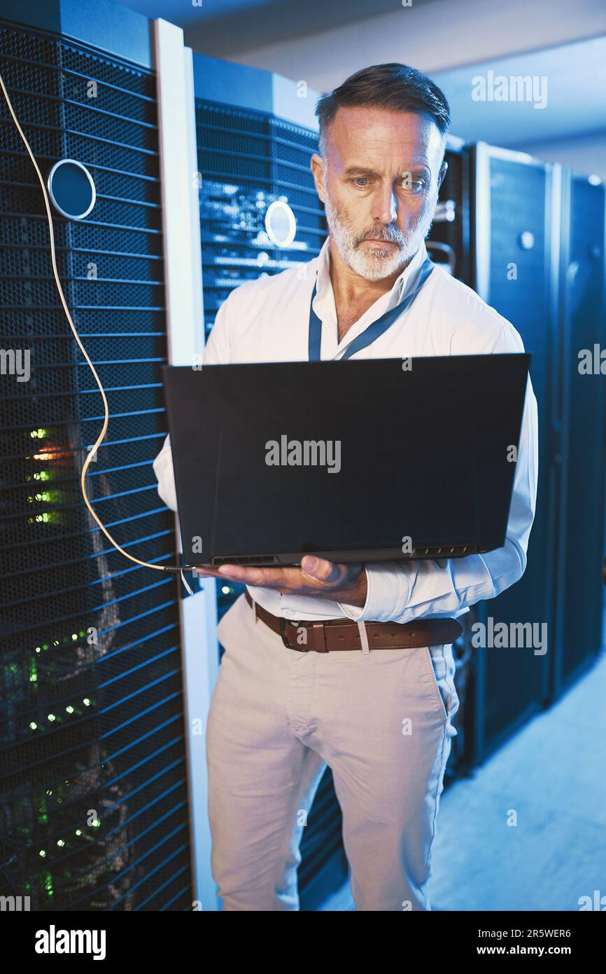 Switching between systems for a quicker connection. a mature man using a laptop while working in a server room. Stock Photo