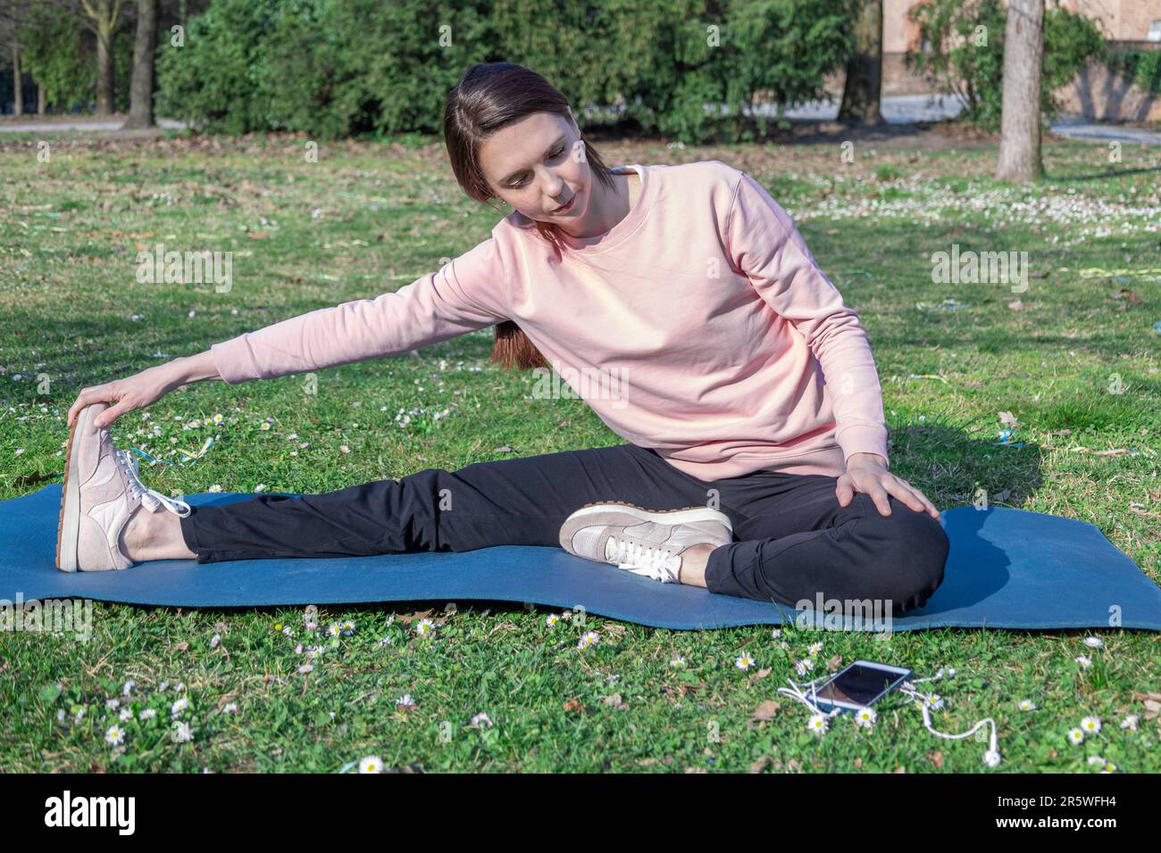 Young woman with long hair doing yoga on mat in the city park. Breathing practices and mental