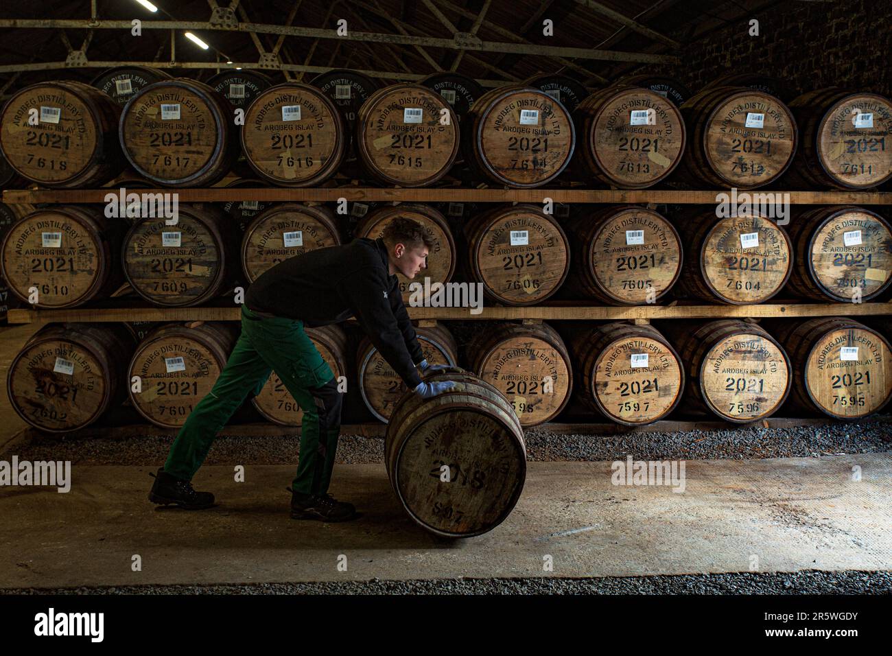 An employee rolls a cask at the warehouse, Ardbeg Distillery, Isle of Islay, Inner Hebrides, Scotland, United Kingdom. Stock Photo