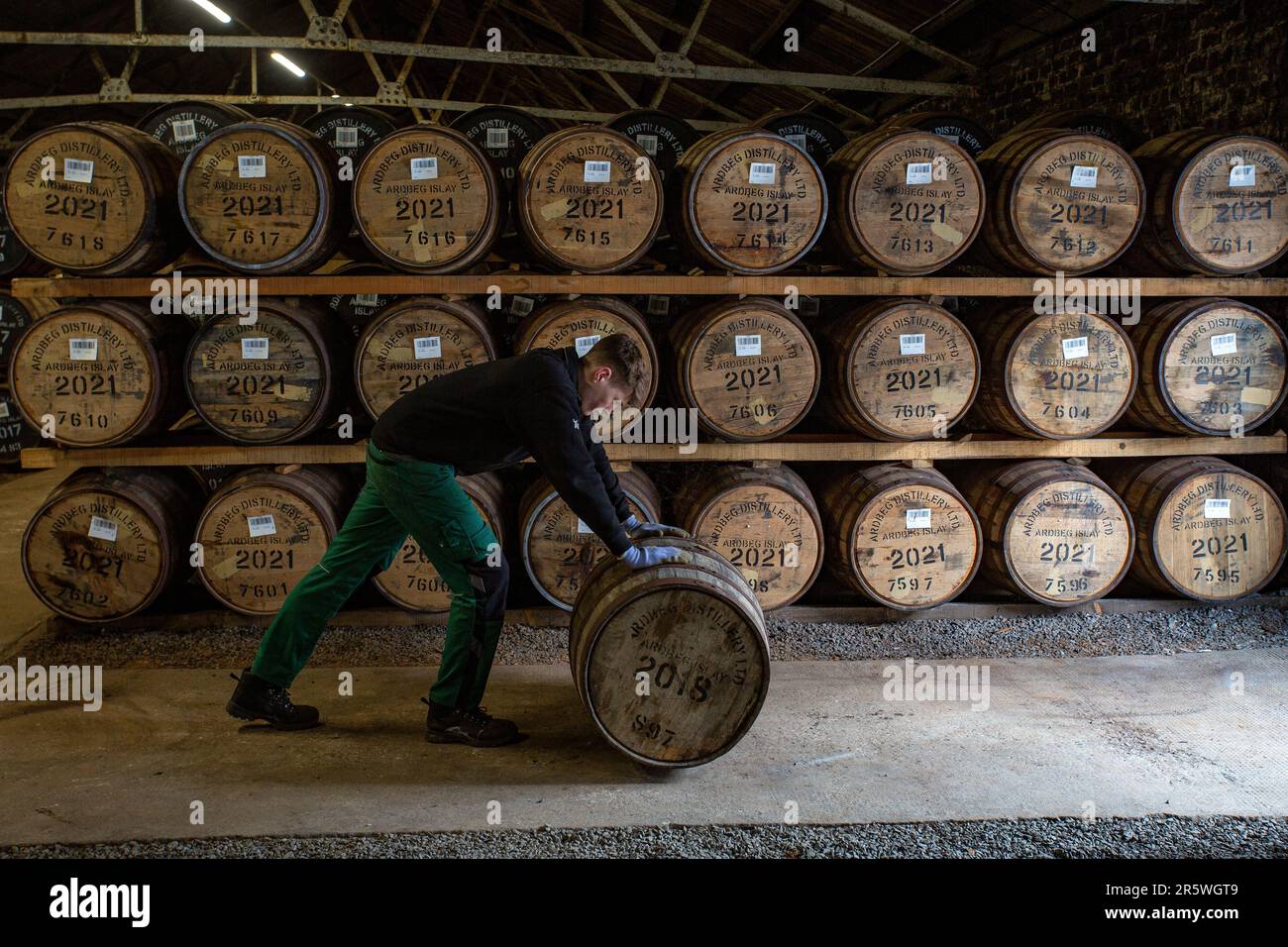 An employee rolls a cask at the warehouse, Ardbeg Distillery, Isle of Islay, Inner Hebrides, Scotland, United Kingdom. Stock Photo