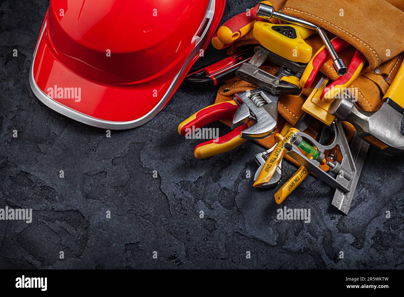 A red Helmet And Construction Tools In Belt On Black Background Stock Photo