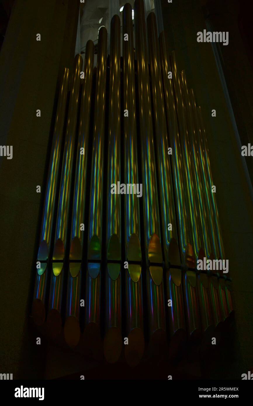 Focus on the pipes of an organ. They are in a colorful church. The reflections are blue, yellow and green. Organs are still used during mass. Stock Photo
