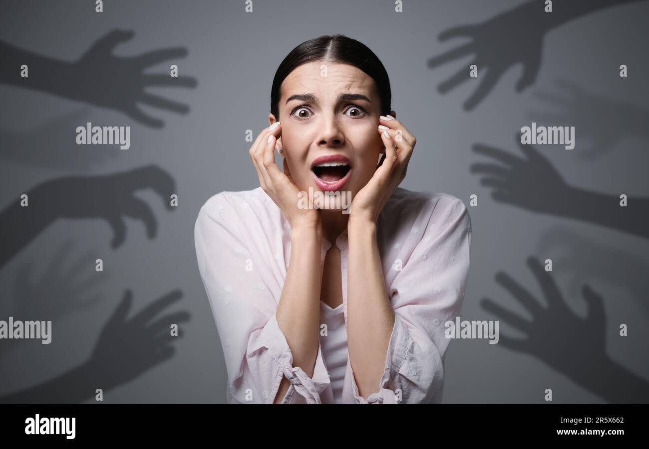 Paranoid delusion. Scared woman screaming on grey background. Shadows of hands reaching for her symbolizing fear and anxiety Stock Photo
